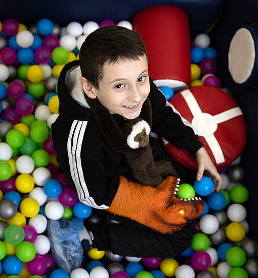 Damir sitzt in einem Raum voller Plastikbälle und spielt damit