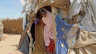 Fanta steht im Eingang einer Unterkunft aus Stroh und Planen.