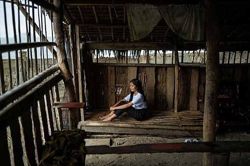 Ein Mädchen im jugendlichen Alter sitz auf einer Bank in einer Unterkunft auf Holzbrettern