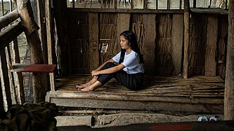 Ein Mädchen im jugendlichen Alter sitz auf einer Bank in einer Unterkunft auf Holzbrettern