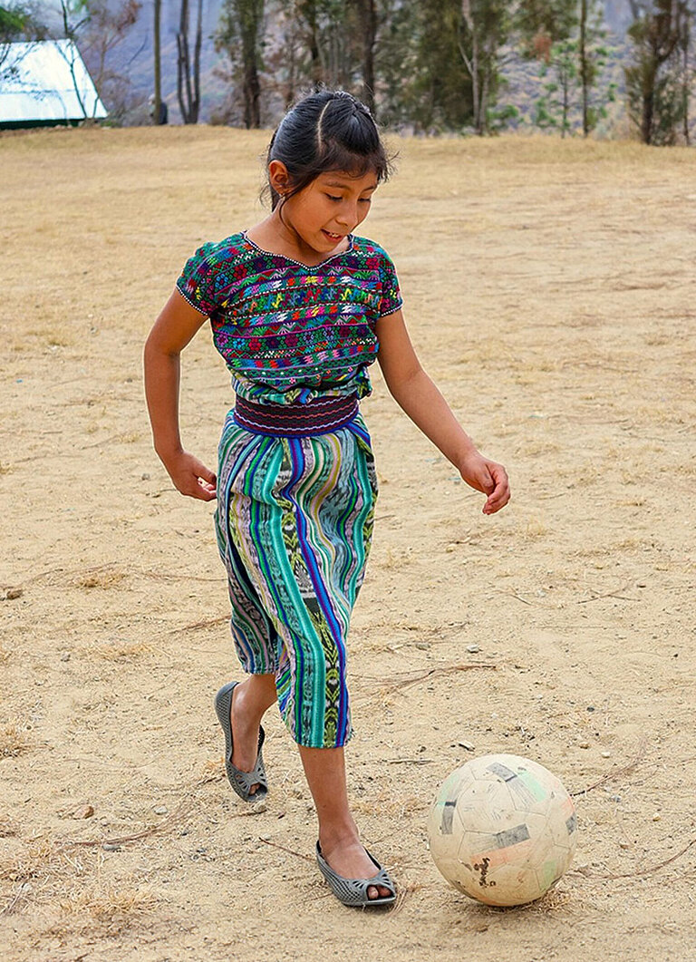 Ein Mädchen kickt einen Fußball über einen staubigen Platz