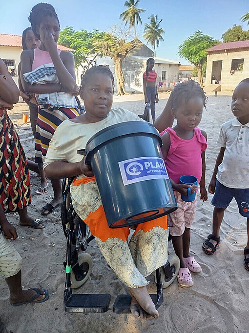 Eine mosambikanische Frau im Rollstuhl hält ein Hygiene-Kit in der Hand