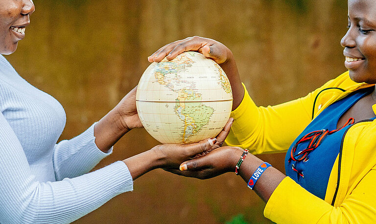 Ein Mädchen in gelber Bluse und ein Mädchen in grauem Pullover halten zusammen eine Weltkugel in ihren Händen