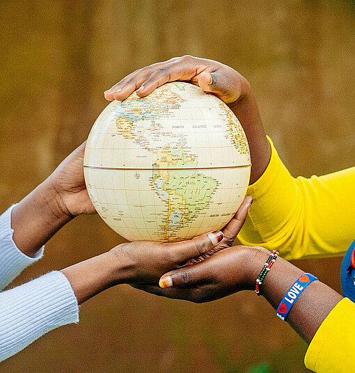 Ein Mädchen in gelber Bluse und ein Mädchen in grauem Pullover halten zusammen eine Weltkugel in ihren Händen
