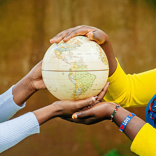 Ein Mädchen in gelber Bluse und ein Mädchen in grauem Pullover halten zusammen eine Weltkugel in ihren Händen