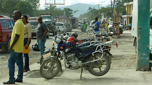 Männer stehen an einer Straße neben Motorrädern.