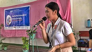 Junge Frau spricht bei einer Peer-Education-Veranstaltung mit Mikrofon – Aufklärung über Kinderhandel auf den Philippinen.