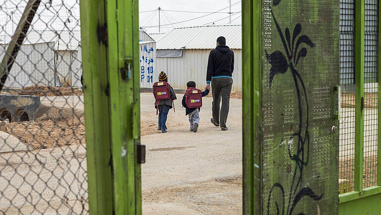 Mann und zwei Kleinkinder hinter einem grünen Gittertor.