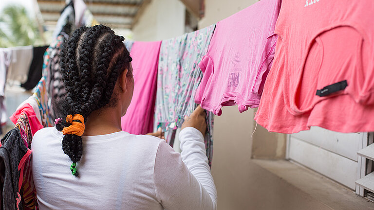 Mädchen hängt pinke T-Shirts an Wäscheleine auf.
