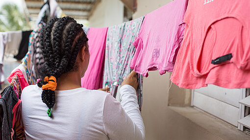Mädchen hängt pinke T-Shirts an Wäscheleine auf.