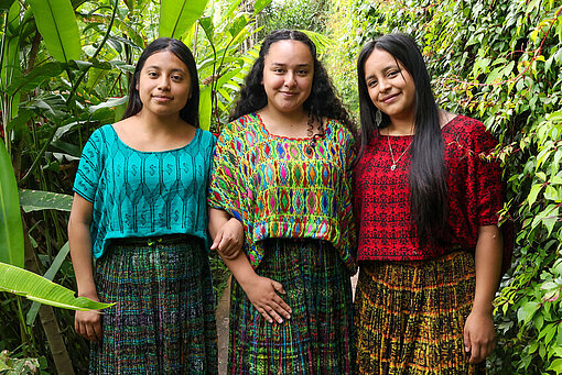 Jaqueline steht zwischen zwei jungen Frauen und lächelt