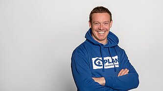 Felix Loch trägt einen Plan International-Hoddie und steht mit verschränkten Armen da. Er lächelt in die Kamera.