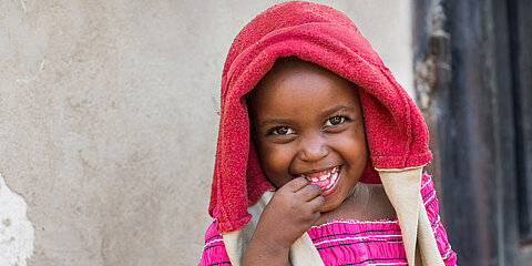 Ein Mädchen trägt einen Pullover über den Kopf und lacht mit offenem Mund in die Kamera. 