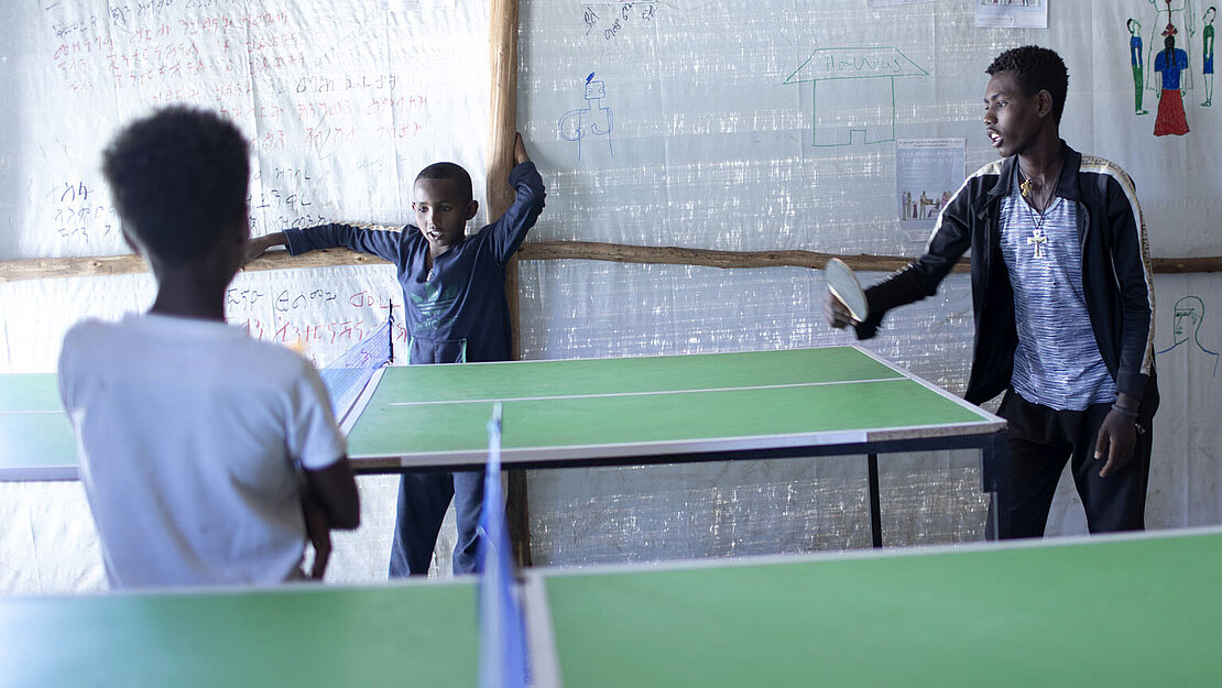 Drei Jungen stehen an einer Tischtennisplatte.