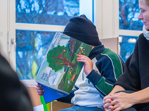 Kind liest ein Heft mit dem Titel „Stark in die Zukunft!“ in einem Klasenraum