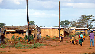 Eine Gruppe Kinder und zwei Erwachsene stehen vor rudimentär gebauten Hütten im Flüchtlingscamp.