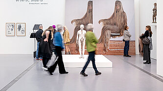 Personen laufen durch einen schneeweißen Raum, an dessen Wänden große Bilder und Fotos hängen