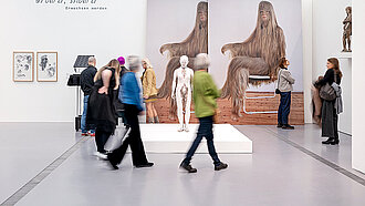 Personen laufen durch einen schneeweißen Raum, an dessen Wänden große Bilder und Fotos hängen