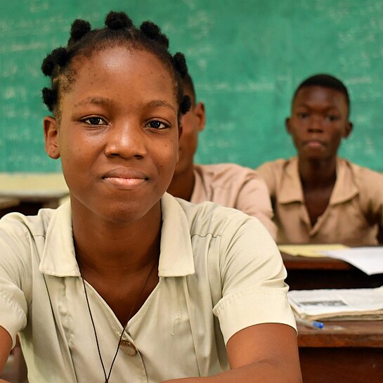 Monique sitzt an ihrem Platz im Klassenzimmer und folgt dem Unterricht