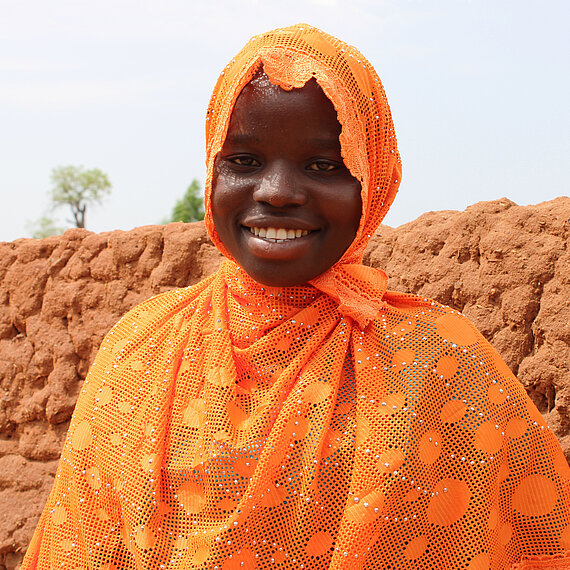 Eine junge Frau mit orangem Kopftuch lächelt in die Kamera