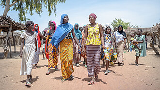 Eine Gruppe Mädchen in bunten Kleidern läuft gemeinsam über einen sandigen Weg