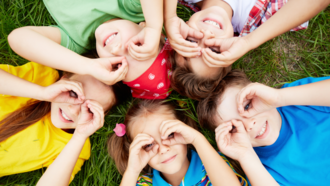 5 Kinder formen Brillen mit ihren Händen und liegen dabei auf dem Rasen