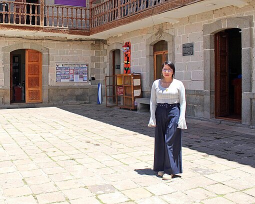 Eine Frau in weißem Pullover und schwarzem Rock steht vor einem Gebäude