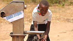 Kind wäscht sich die Hände an einer Wasserpumpe mit Plan-Logo in Malawi