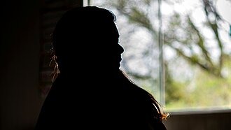 Eine Silhouette einer Frau vor einem Fenster sitzend.