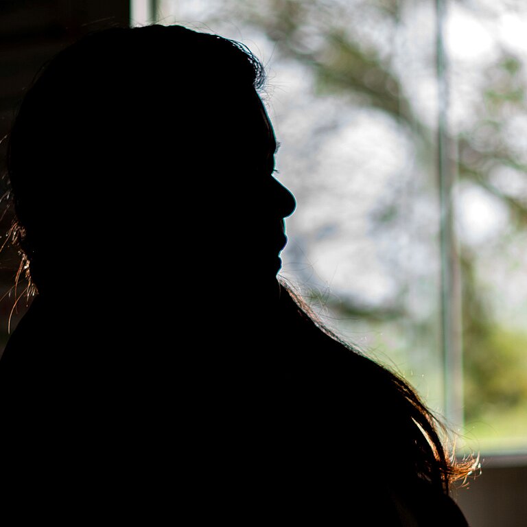 Eine Silhouette einer Frau vor einem Fenster sitzend.