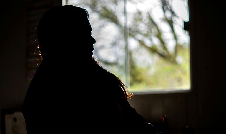 Eine Silhouette einer Frau vor einem Fenster sitzend.
