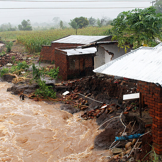 Reißende Wassermassen, daneben zerstörte Häuser