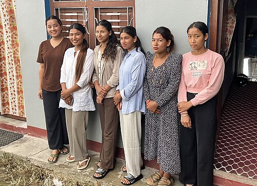 Sechs junge Frauen stehen vor einem Haus und lächeln in die Kamera.