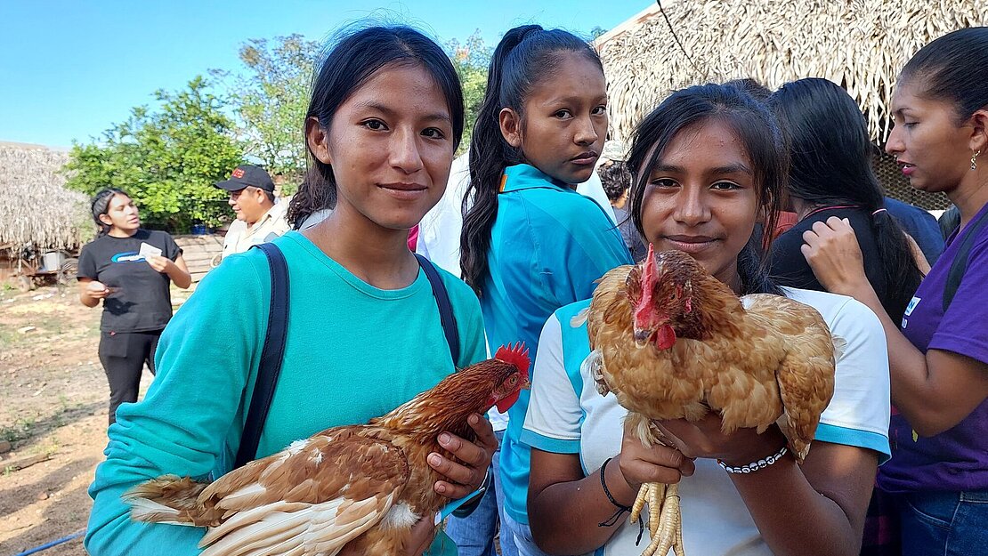 Zwei Teenagerinnen haben jeweils ein Huhn auf dem Arm und lächeln stolz.