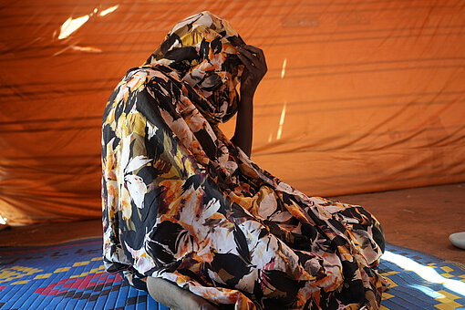 Eine sudanesische Frau sitzt auf dem Boden und hat den Kopf in die Hände gestützt