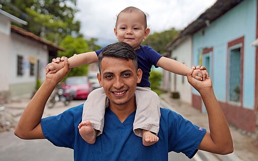 Als junger Vater verbringt Steven mehr Zeit mit seinem Sohn Ein Mann trägt seinen lachenden Sohn auf den Schultern