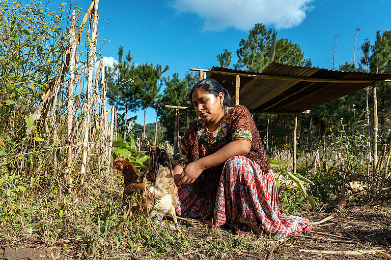 Eine Frau kniet neben einem Huhn in ihrem Garten.