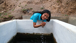Mädchen nutzt sauberes Trinkwasser aus einem Wasserbecken in einer ländlichen Gemeinde in Bolivien