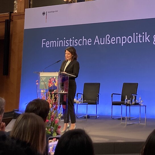 Ministerin Baerbock steht auf einer Bühne und spricht. Im Hintergrund steht der Schriftzug "Feministische Außenpolitik"