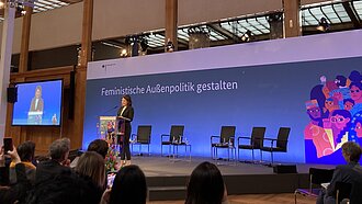 Auf dem Bild steht Ministerin Annalena Baerbock auf der Bühne und spricht zu einem Publikum. Im Hintergrund steht der Schriftzug "Feministische Außenpolitik gestalten"