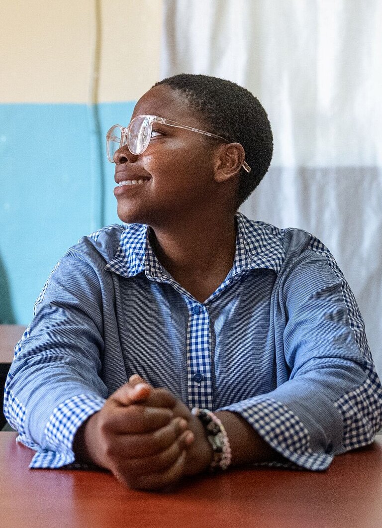 Ein junges Mädchen mit Brille schaut zur Seite und lächelt