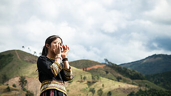 Ein Mädchen steht vor einer Hügellandschaft. Sie hält ihre Hände wie einen Verstärker geformt vor ihren Mund.