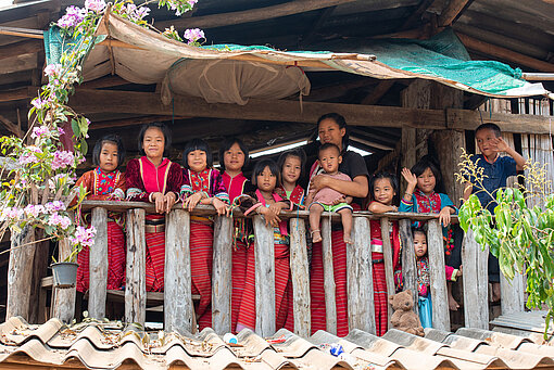 Eine Familie mit vielen Kindern steht auf einem Balkon. Einige Kinder winken zur Kamera.