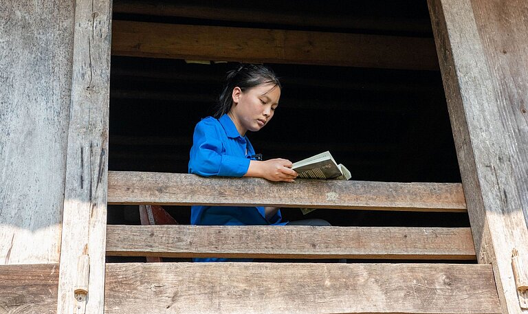 Ein vietnamesisches Mädchen sitzt am Fenster und liest ein Buch