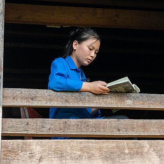 Ein vietnamesisches Mädchen sitzt am Fenster und liest ein Buch
