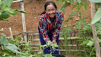 Win, eine junge Frau aus Laos, gießt ihren Gemüsegarten. 