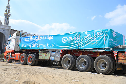Lastwagen mit Plan International Banner fährt mit Hilfsgütern für Kinder in Gaza vor einer Moschee