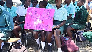 Schülerinnen in Simbabwe halten ein pinkes Plakat mit der Aufschrift „Give us education, not husbands“ als Zeichen gegen Kinderheirat.