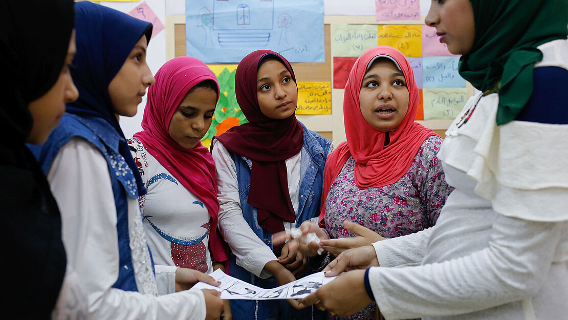 Eine Gruppe junger Frauen steht beisammen. Sie halten ein Blatt Papier in der Hand und diskutieren.