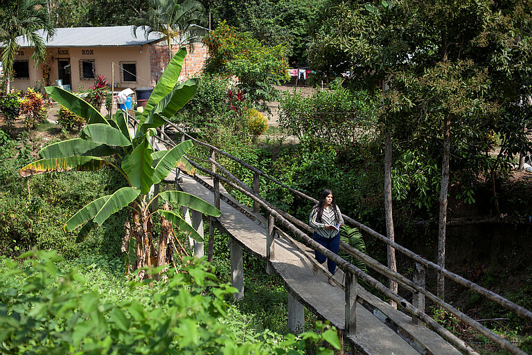 Eine schmale Fußgängerbrücke führt durch grünen Wald, eine junge Frau läuft über die Brücke